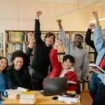 group of people smiling and standing near brown wooden table raising hands