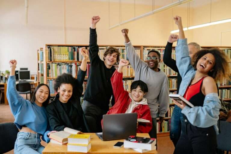 group of people smiling and standing near brown wooden table raising hands