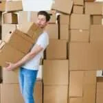 young man carrying heap of cardboard boxes during relocation in new flat
