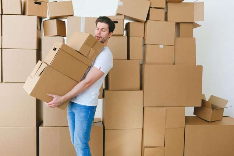 young man carrying heap of cardboard boxes during relocation in new flat